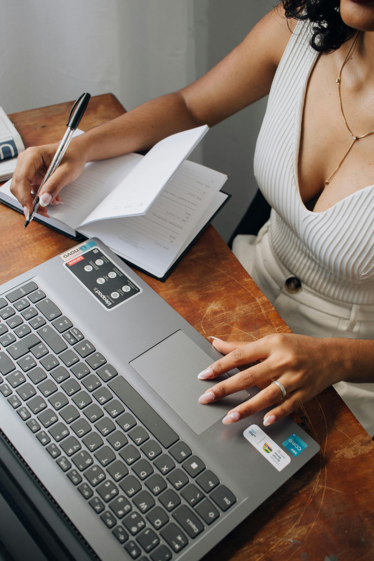 Frau schreibt in ein Notizbuch und arbeitet am Laptop – NutsAndNotes bietet Flexibilitaet und Langlebigkeit.
