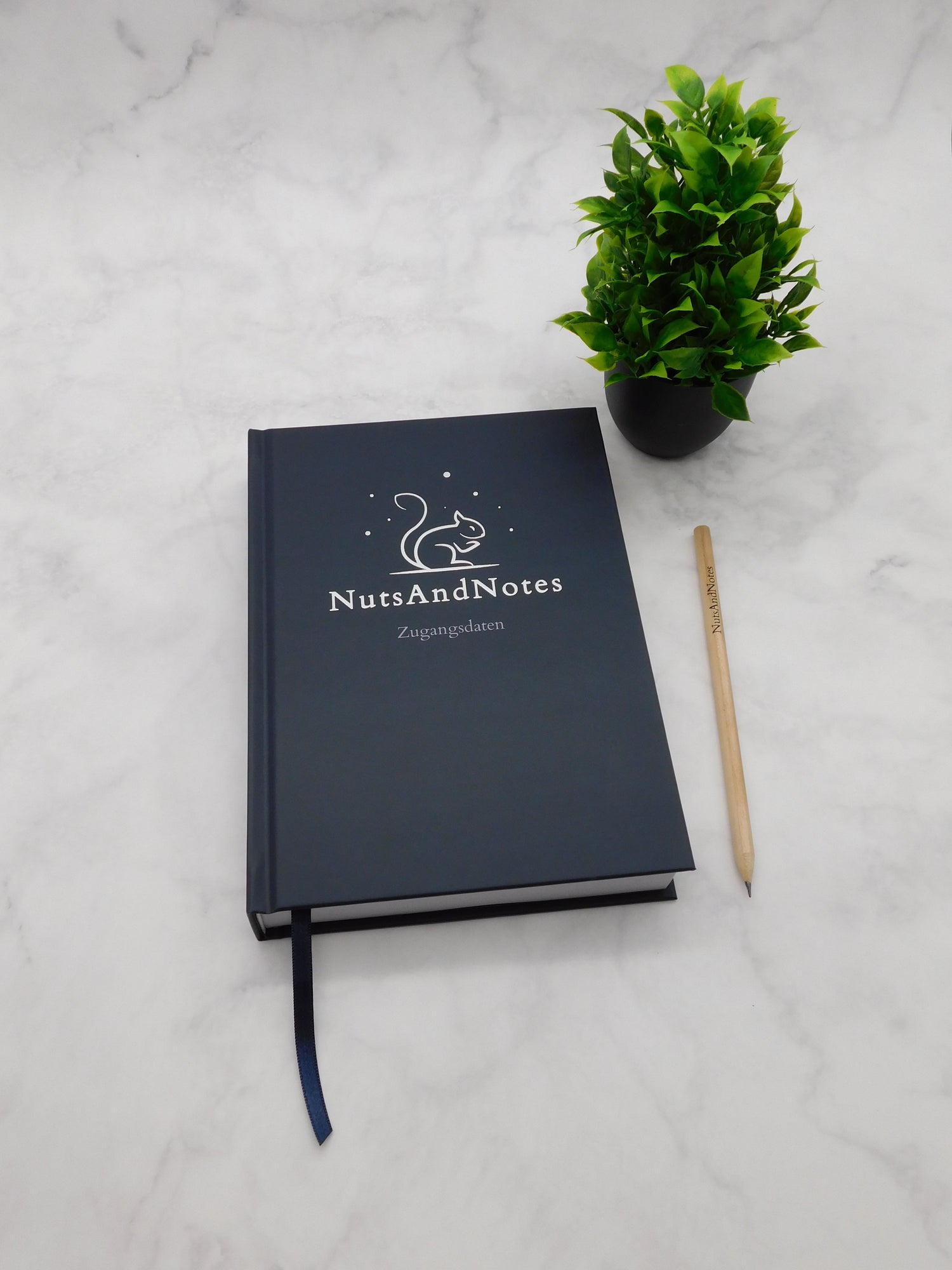 NutsAndNotes Zugangsdaten mit Pflanze und Holzstift auf Marmorhintergrund – Passwortmanager in elegantem Design.